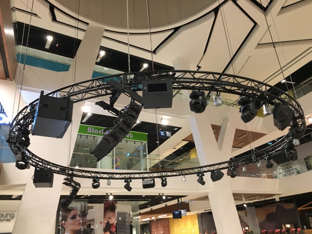 Indoor view of MyTown Shopping Centre with circular truss system carrying various sizes of speakers and lighting systems